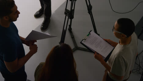 Overhead-Shot-Of-Film-Director-Talking-With-Male-And-Female-Actors-Holding-Scripts-Rehearsing-For-Shooting-Movie-Or-Video-In-Studio